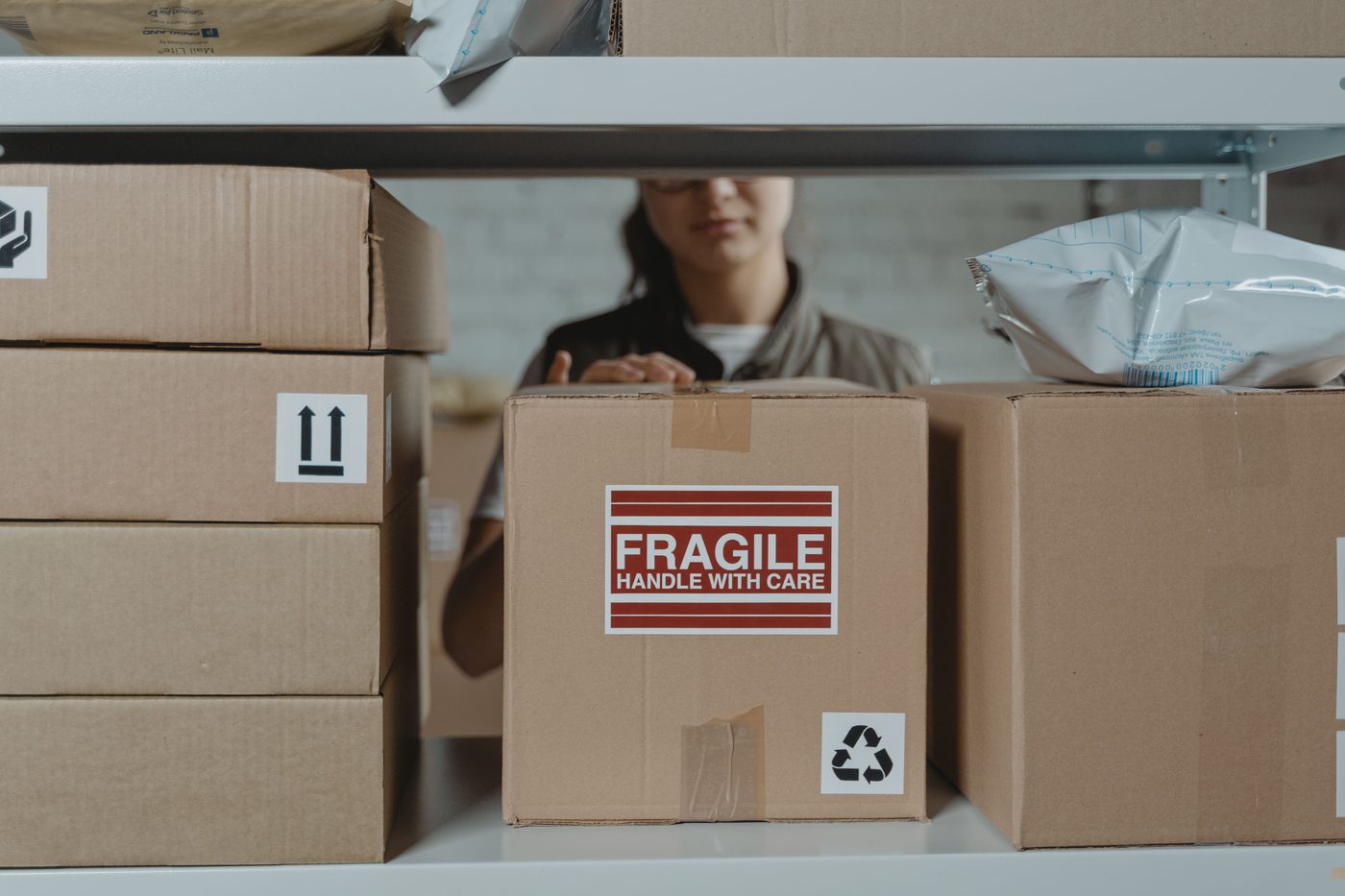 Fulfillment associate preparing a labelled fragile carton for shipment on a warehouse shelving unit